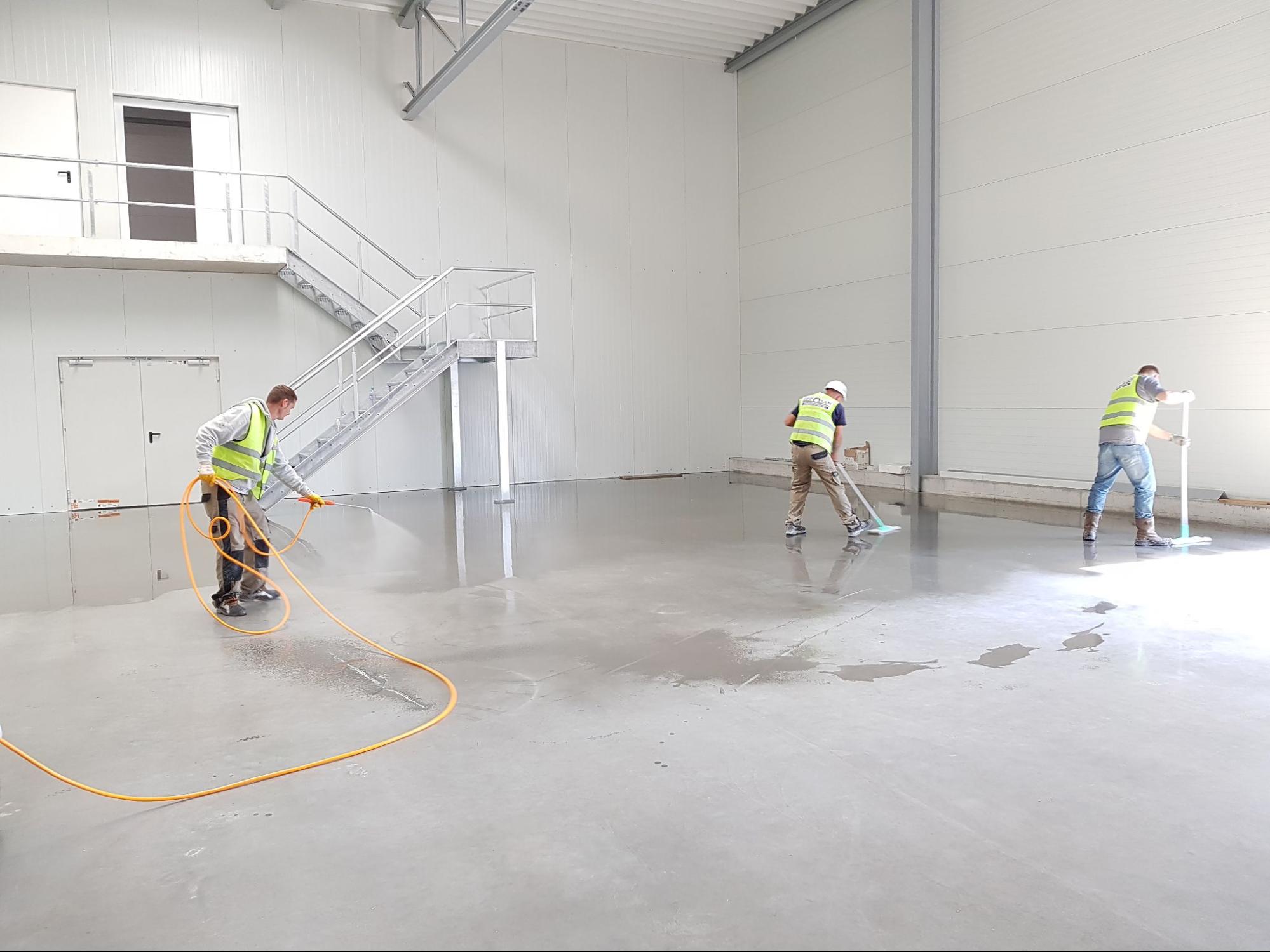 An image of three men cleaning an empty room in a large facility
